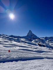 Scenic winter landscape with the matterhorn under a clear blue sky. Bright sun, fresh snow, and alpine terrain create a dramatic view of the Swiss Alps.