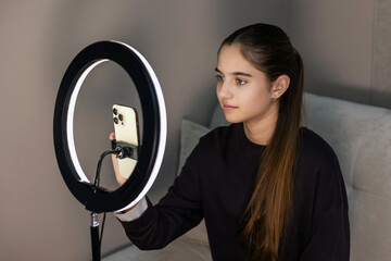 Teen girl filming video with ring light. Teenage girl using a smartphone and ring light setup, recording video content at home, possibly for social media or vlog.