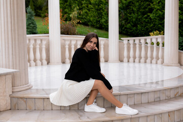 Elegant young woman sitting on marble steps in a serene garden setting during a sunny day