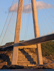 Obraz premium Cable-stayed bridge illuminated by warm sunset light, with tall pylons and suspension cables creating strong geometric lines. A mix of modern architecture and natural landscape. 