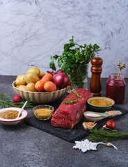 Ingredients for Christmas roast beef with carrots, potatoes, and onions on a dark concrete background. Hot holiday dishes. Merry Christmas.