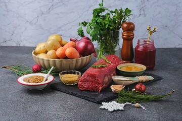 Ingredients for Christmas roast beef with carrots, potatoes, and onions on a dark concrete background. Hot holiday dishes. Merry Christmas.