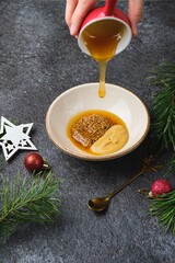 Mixing grainy and Dijon mustard with honey for a glaze on roast beef or other meats against a dark background in Christmas decor.