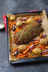 A roast beef loin on a baking sheet with carrots, onions, and potatoes. Cooking beef in the oven as a whole piece. Merry Christmas.
