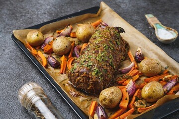 A roast beef loin on a baking sheet with carrots, onions, and potatoes. Cooking beef in the oven as a whole piece. Merry Christmas.