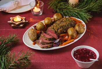 Cooked roast beef with carrots and onions on a white platter on a festive Christmas table setting. Merry Christmas! Beef dishes.