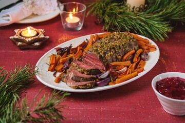 Cooked roast beef with carrots and onions on a white platter on a festive Christmas table setting. Merry Christmas! Beef dishes.
