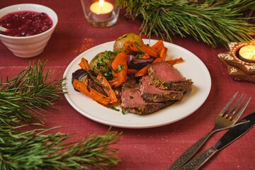 A serving of roast beef with potatoes, carrots, and onions on a white plate on a festive Christmas table setting. Merry Christmas! Beef dishes.