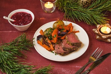 A serving of roast beef with potatoes, carrots, and onions on a white plate on a festive Christmas table setting. Merry Christmas! Beef dishes.