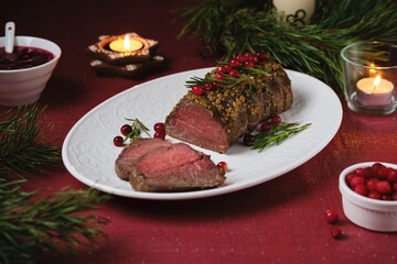 Beef tenderloin rolls garnished with cranberries and rosemary on a white platter on a festive Christmas table setting. Served with cranberry sauce. Merry Christmas. Step-by-step recipes.
