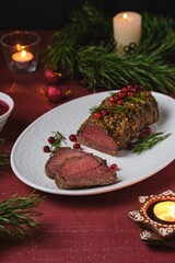 Beef tenderloin rolls garnished with cranberries and rosemary on a white platter on a festive Christmas table setting. Served with cranberry sauce. Merry Christmas. Step-by-step recipes.