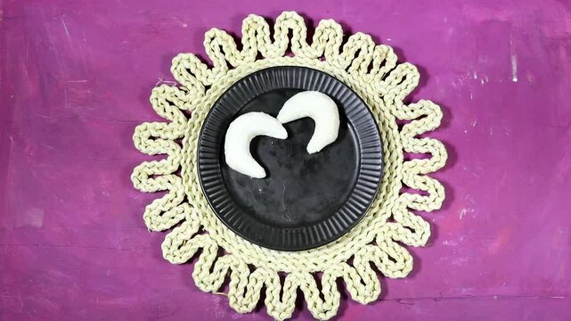 Oriental Algerian sweet cookies named tcharek aryen in arabic which mean almond cookies in english  On Black Plate With Hands, Rustic Woven Mat 