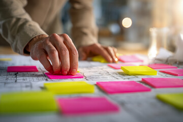 Person organizing colorful sticky notes on architectural blueprints in a creative planning and brainstorming session at a workspace with natural light