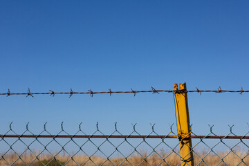 Barbed wire fence against blue sky. Symbol of prison, border protection, safety, defense, and immigration control