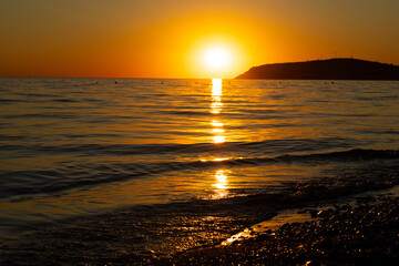 Mediterranean harbor at sunset in Albania. Orange sky over blue sea, waves and mountain. Concept of travel, tourism and vacation