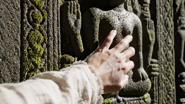 Hand Touches Stone Carving at Ancient Temple Wall in Sunlight