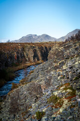 Storslåttfossen waterfall flowing through rocky canyon with Rondane peaks in Norway