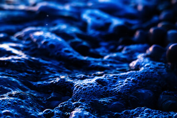 Closeup sea foam and bubbles on blue water surface. Abstract cool ocean background, natural macro texture for summer, travel, refreshment and nature concepts