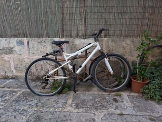 Two old neglected unmaintained mountain bikes by rustic stone wall on paved Mallorcan patio. Dirty abandoned bicycles with rust and wear. Urban decay, upcycling, bike repair, junk, forgotten, broken. 