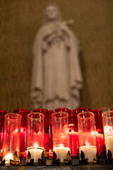 Cierges rouge et banc et statue derrière, floue, intérieur vertical.