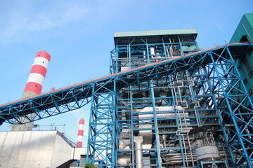 Detailed power plant structure with chimney against the vibrant blue sky backdrop.