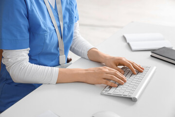 Female doctor working with computer at table in clinic, closeup