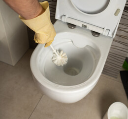 Close-up of a person cleaning a toilet bowl  while wearing protective rubber gloves, illustrating hygiene, sanitation, and household cleaning