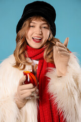 Smiling young woman in winter clothes with mulled wine on blue background, closeup