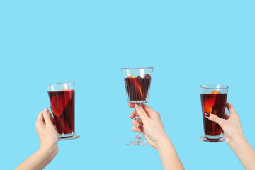 Female hands with glasses of warm mulled wine on blue background