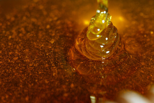 Golden honey dripping slowly into a pool of amber liquid, showcasing the smooth texture and rich color, highlighting the natural sweetness and culinary versatility of honey