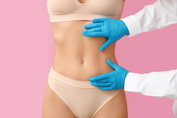 Young woman with flat belly and plastic surgeon on pink background, closeup