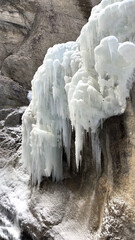 A dramatic winter scene shows pale icicles and frozen formations clinging to a rugged cliff Partnachklamm. The icy cascade above shallow pool captures cold, silent, natural beauty in rugged landscape.