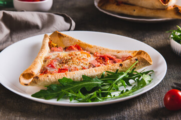 Egg, sausage and tomatoes baked in a triangular tortilla on a plate on the table