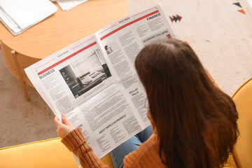 Naklejka premium Young woman reading newspaper on sofa at home, top view