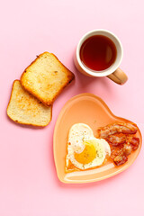 Plate with fried egg, tasty bacon, toasts and cup of tea on pink background