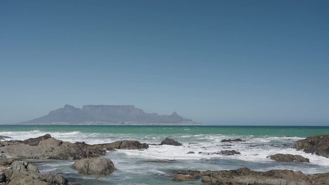 Waves break onto Blouberg shore, with stunning views of Table Mountain, Devil&rsquo;s Peak, and Signal Hill in Cape Town, Western Cape, South Africa. Perfect coastal nature footage in 4K 30fps.
