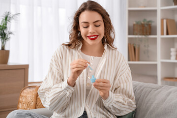 Beautiful young happy woman with bottle of nail polish in living room