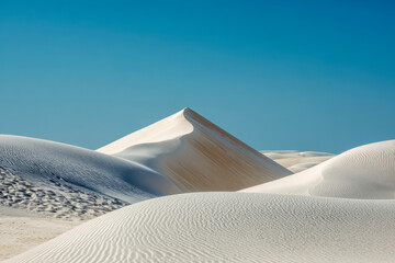 Expansive white sand dunes under a clear blue sky showcasing smooth curves and sharp ridges in a serene desert landscape scene