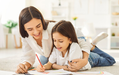 Happy mother and child drawing a picture together. Smiling little girl together with mom lying on...