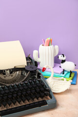 Vintage typewriter and knitted toys on table near purple wall