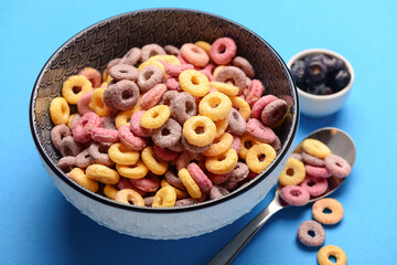 Bowls with colorful sweet cereal rings and blueberries on blue background