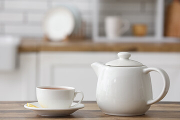 White teapot and cup of tea on wooden table in kitchen