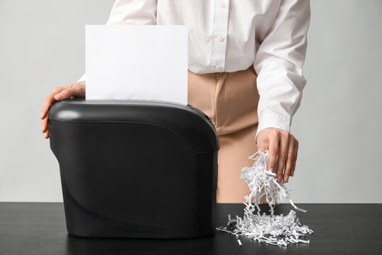 Secretary destroying document in shredder on light background