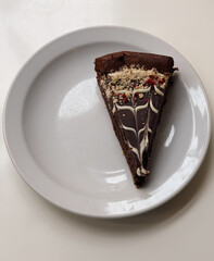 Slice of chocolate tart with nuts and ganache on white plate 
