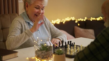 Positive woman in her 80s playing chess with husband, memory training activity - Powered by Adobe