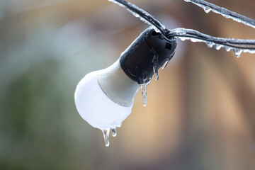 Close-up of a frozen light bulb with icicles hanging from a wire, showcasing a wintery scene with a...