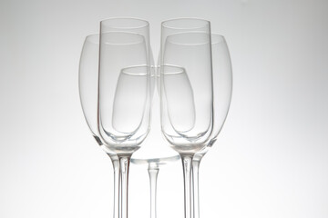 Five stylish wine glasses with unique contours, their reflections mirrored on a polished surface, set against a subtle gray background for upscale settings.