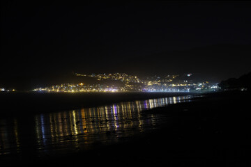 Night cityscape with lights reflecting on wet beach sand and dark sky