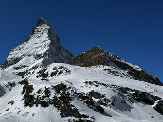 Winter view of the iconic Matterhorn peak covered in snow under a clear blue sky in the Swiss Alps. High-resolution mountain landscape ideal for travel, nature and winter sports themes.