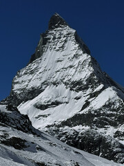 Winter view of the iconic Matterhorn peak covered in snow under a clear blue sky in the Swiss Alps. High-resolution mountain landscape ideal for travel, nature and winter sports themes.